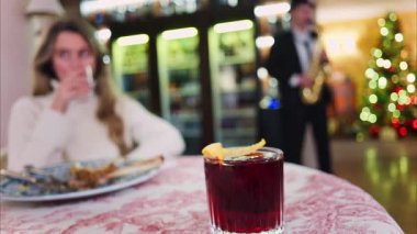 Kırmızı ve beyaz bir masa örtüsü üzerine negroni kokteyli yakın plan arkasında bir restoranda oturan bir kadın