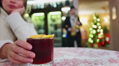 Arka planda Noel ağacı olan bir restoranda kırmızı ve beyaz masa örtüsü üzerinde negroni kokteyli tutan bir kadının fotoğrafını çek.