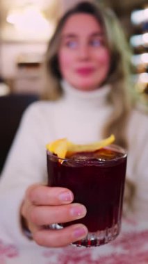 Lokantada kırmızı beyaz masa örtüsüne negroni kokteyli koyan bir kadının yakın plan fotoğrafı. Dikey