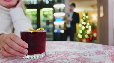 Arka planda Noel ağacı olan bir restoranda kırmızı ve beyaz masa örtüsü üzerinde negroni kokteyli tutan bir kadının fotoğrafını çek.