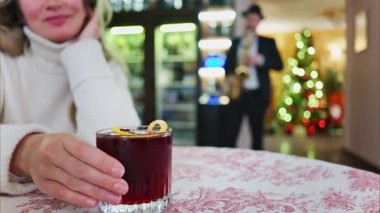Arka planda Noel ağacı olan bir restoranda kırmızı ve beyaz masa örtüsü üzerinde negroni kokteyli tutan bir kadının fotoğrafını çek.