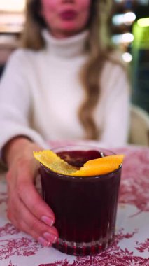 Lokantada kırmızı beyaz masa örtüsüne negroni kokteyli koyan bir kadının yakın plan fotoğrafı. Dikey