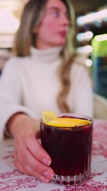 Lokantada kırmızı beyaz masa örtüsüne negroni kokteyli koyan bir kadının yakın plan fotoğrafı. Dikey