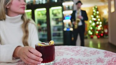 Arka planda Noel ağacı olan bir restoranda kırmızı ve beyaz masa örtüsü üzerinde negroni kokteyli tutan bir kadının fotoğrafını çek.