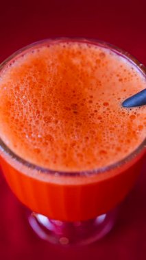 Portakal suyu ve havuç suyunu kırmızı masa örtüsünün üzerinde siyah bir pipetle bardağa doldur. Dikey