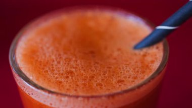 Portakal suyu ve havuç suyunu kırmızı masa örtüsünün üzerinde siyah bir pipetle bardağa koy.