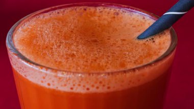 Portakal suyu ve havuç suyunu kırmızı masa örtüsünün üzerinde siyah bir pipetle bardağa koy.