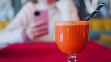 Portakal suyu ve havuç suyunu kırmızı bir masa örtüsünün üzerinde siyah bir kamışla birlikte arka planda bir kadınla bardakta kapat.