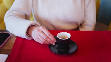 Lokantada kırmızı bir masa örtüsünün üzerinde siyah bir fincanda espresso tutan bir kadının fotoğrafını çek.