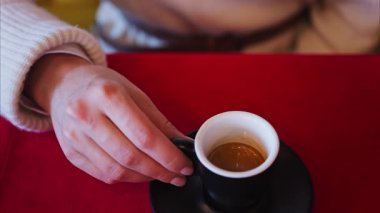 Lokantada kırmızı bir masa örtüsünün üzerinde siyah bir fincanda espresso tutan bir kadının fotoğrafını çek.