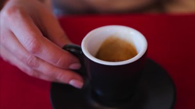 Lokantada kırmızı bir masa örtüsünün üzerinde siyah bir fincanda espresso tutan bir kadının fotoğrafını çek.
