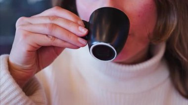 Lokantadaki kırmızı bir masa örtüsünün üzerinde siyah bir bardaktan espresso içen bir kadının fotoğrafını çek.