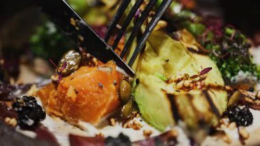 Lokantada ızgara avokado, tatlı patates ve brokoli ile salata yiyen bir kadının yakın plan fotoğrafı.