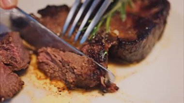 Biberiyeli bifteği bir restoranda beyaz bir tabakta doğrayan bir kadının yakın çekimi.