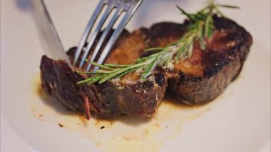 Biberiyeli bifteği bir restoranda beyaz bir tabakta doğrayan bir kadının yakın çekimi.