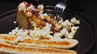 Lokantada siyah bir tabakta muzlu ve karamelli patlamış mısırla cheesecake kesen bir kadına yaklaş.