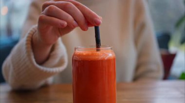 Bir kadının portakal ve havuç suyunu, tahta bir masada siyah bir pipetle karıştırdığı yakın plan.