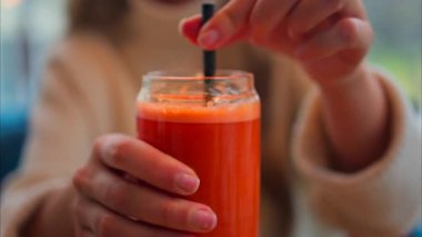 Bir kadının portakal ve havuç suyunu, tahta bir masada siyah bir pipetle karıştırdığı yakın plan.