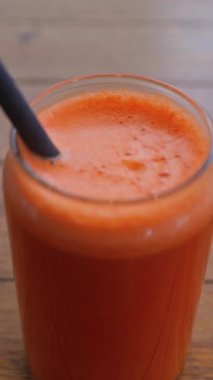 Portakal suyu ve havuç suyunu bir bardakta, tahta bir masada siyah bir pipetle kapat. Dikey