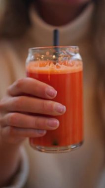 Bir kadının portakal ve havuç suyunu tahta bir masada siyah bir pipetle içerken yakın plan fotoğrafı. Dikey