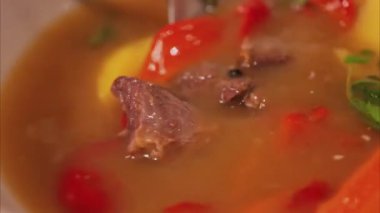 Bir kaşık et suyu, kırmızı dolma biber, sarı patates ve bitkilerle karıştırılmış.