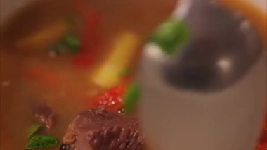 Bir kaşık et suyu, kırmızı dolma biber, sarı patates ve bitkilerle karıştırılmış.