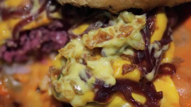 Dolu bir hamburgeri eritilmiş peynir, karamelli soğan ve kızarmış ekmeğin üzerine kremalı sos ile kapat.