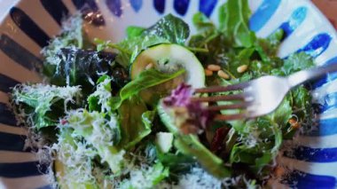 Bir çatalın üzerine yeşil yapraklı ve rendelenmiş parmesan soslu salata al.