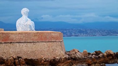 Fransa 'nın Antibes şehrinde akşam saatlerinde Jaume Plensa' nın Göçebe şehir heykelinin uzaktan görünüşü