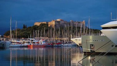 Fransa 'nın Antibes şehrinde günbatımında arka planda Fort Carre ile Vauban Limanı' na yanaşan tekneler.