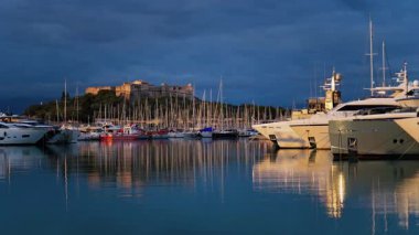 Fransa 'nın Antibes şehrinde günbatımında arka planda Fort Carre ile Vauban Limanı' na yanaşan tekneler.