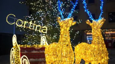 Aydınlatılmış ren geyiği dekorasyonu, İtalya 'nın Cortina d' Ampezzo şehrindeki Noel pazarında kızağa rehberlik ediyor.