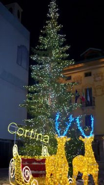 Aydınlatılmış ren geyiği dekorasyonu, İtalya 'nın Cortina d' Ampezzo kentindeki Noel pazarında kızağa rehberlik ediyor. Dikey
