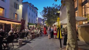 Antibes, Fransa - 13 Ağustos 2024: İnsanlar akşam saatlerinde kentin sokaklarındaki açık kafelerin yakınında yürüyorlar