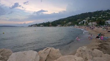 Golfe Juan, Fransa - 14 Ağustos 2024: İnsanlar gün batımında bulutlu bir günde Golfe-Juan kasabasında plajda dinleniyor