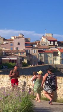 Antibes, Fransa - 20 Temmuz 2024: Kıyıdaki farklı binaların etrafında yürüyen insanları görmek. Dikey
