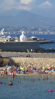 Antibes, Fransa - 20 Temmuz 2024: Denizde yüzen ve plajda dinlenen insanları görmek. Dikey