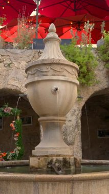 Saint Paul de Vence, Fransa - 10 Ağustos 2024: Saint Paul de Vence, Fransa 'da üzerinde kırmızı şemsiyeler bulunan bir su çeşmesinin manzarası. Dikey