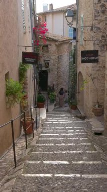 Saint Paul de Vence, Fransa - 10 Ağustos 2024: Şehrin dar, kaldırımlı bir sokağındaki dükkanların manzarası. Dikey