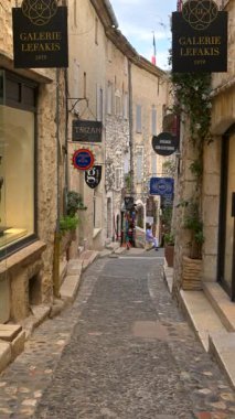 Saint Paul de Vence, Fransa - 10 Ağustos 2024: Şehrin dar, kaldırımlı bir sokağındaki dükkanların manzarası. Dikey