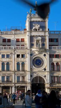 Venedik, İtalya - 18 Ocak 2025: St. Mark Meydanı 'ndaki Saat Kulesi' nin önünde yürüyen insanlar. Dikey