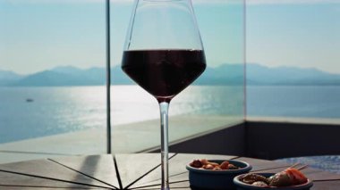 Bir bardak kırmızı şarap ve bir terasta deniz manzaralı aperatifleri kapatın.