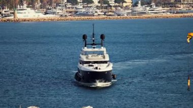 Cannes, Fransa - 16 Mart 2025: Güneşli bir günde arka planda liman olan beyaz bir tekne denizde hareket ediyor