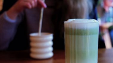 Arka planda bir kafedeki masada içki içen bir kadınla matcha latte iç.