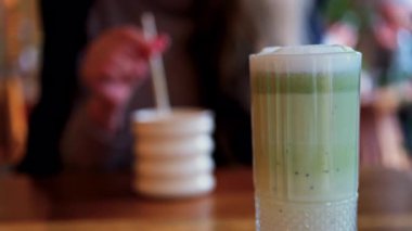 Arka planda bir kafedeki masada içki içen bir kadınla matcha latte iç.