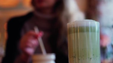 Arka planda bir kafedeki masada içki içen bir kadınla matcha latte iç.