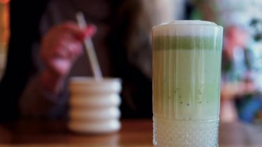 Arka planda bir kafedeki masada içki içen bir kadınla matcha latte iç.