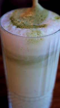 Bir kafede, bir kibrit sütlü kahveye karıştırılmış pipetin yakın çekim görüntüsü. Dikey