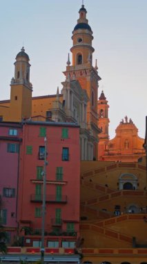 Menton, Fransa - 18 Mart 2025: St. Michel Bazilikası 'nın renkli binalarla çevrili uzak manzarası. Dikey