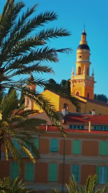 Menton, Fransa - 18 Mart 2025: Renkli binalar ve palmiye ağaçları ile çevrili Aziz Michel Bazilikası 'nın uzak manzarası. Dikey